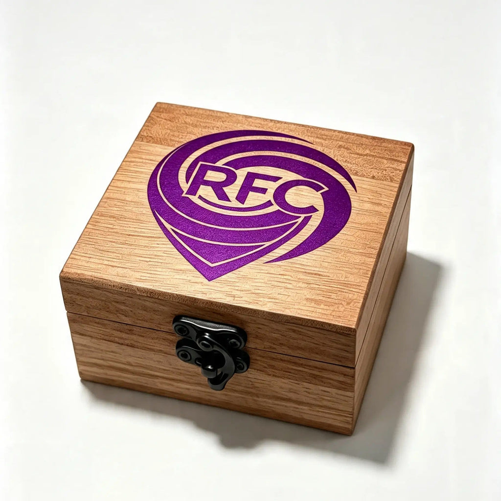 A square wooden keepsake box with a black metal latch, featuring a purple 'RFC' logo printed on the lid, set against a plain white background.